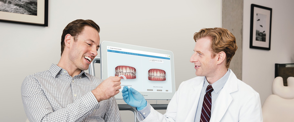 Person in white coat and blue glove handing dental appliance to smiling patient.