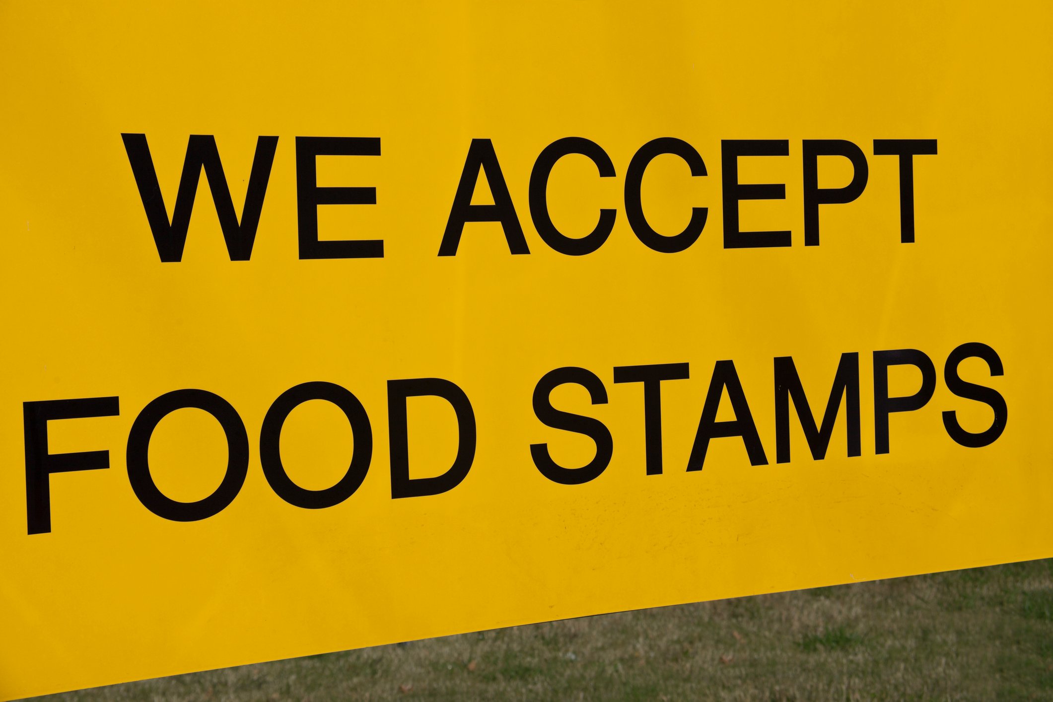 Gold sign with black lettering reads We Accept Food Stamps