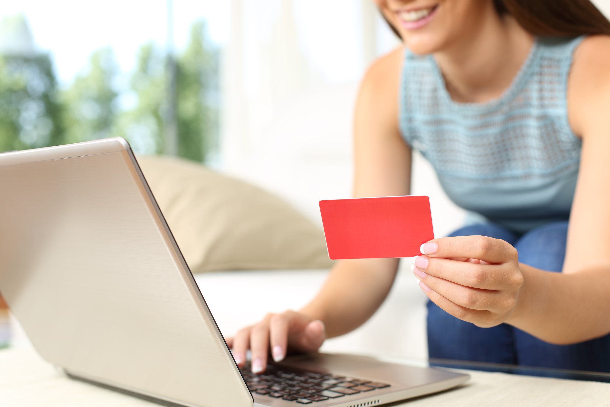 A smiling woman holds a red credit card next to her laptop.