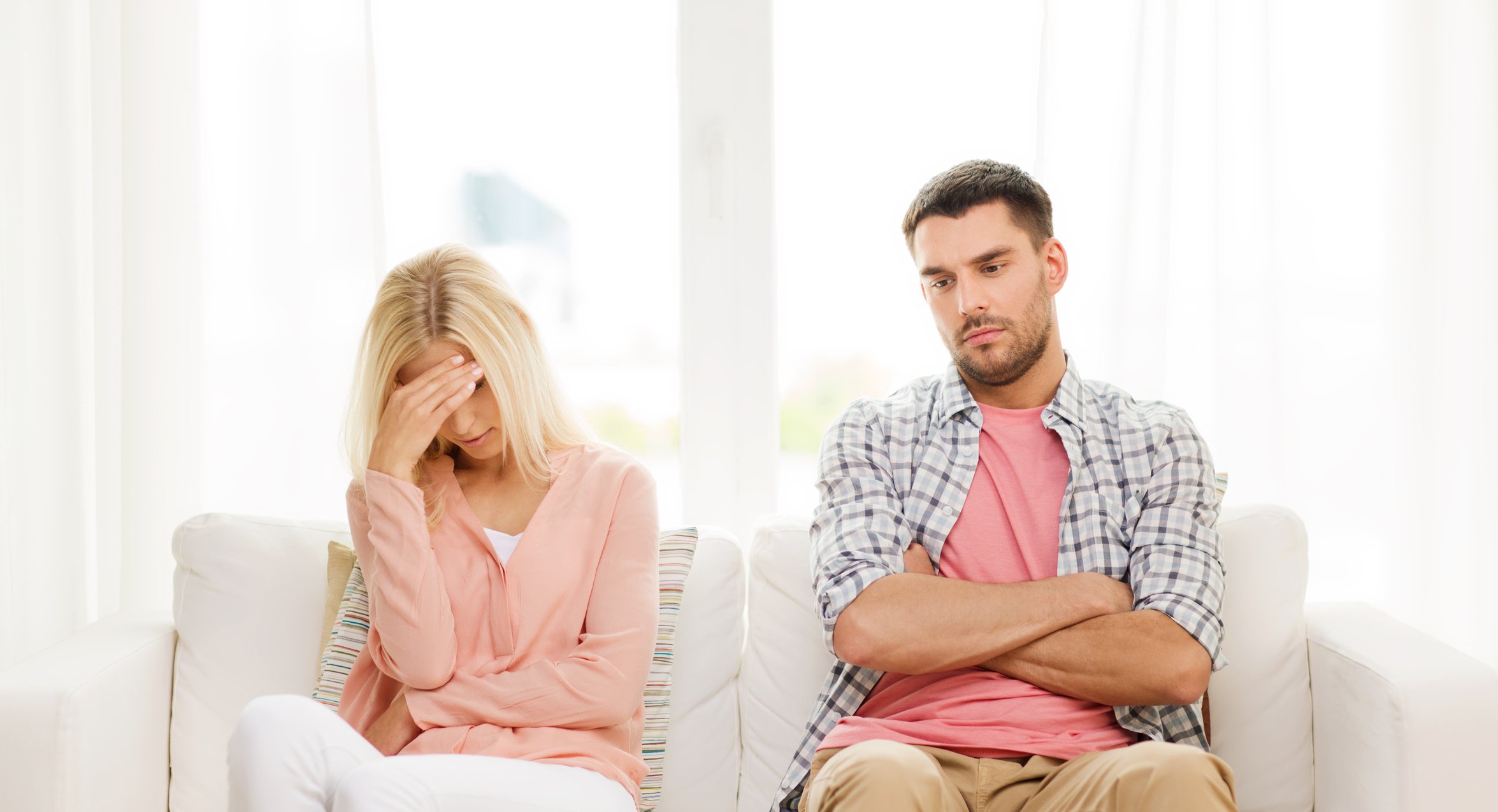 Two people sit on a couch looking angry and sad.