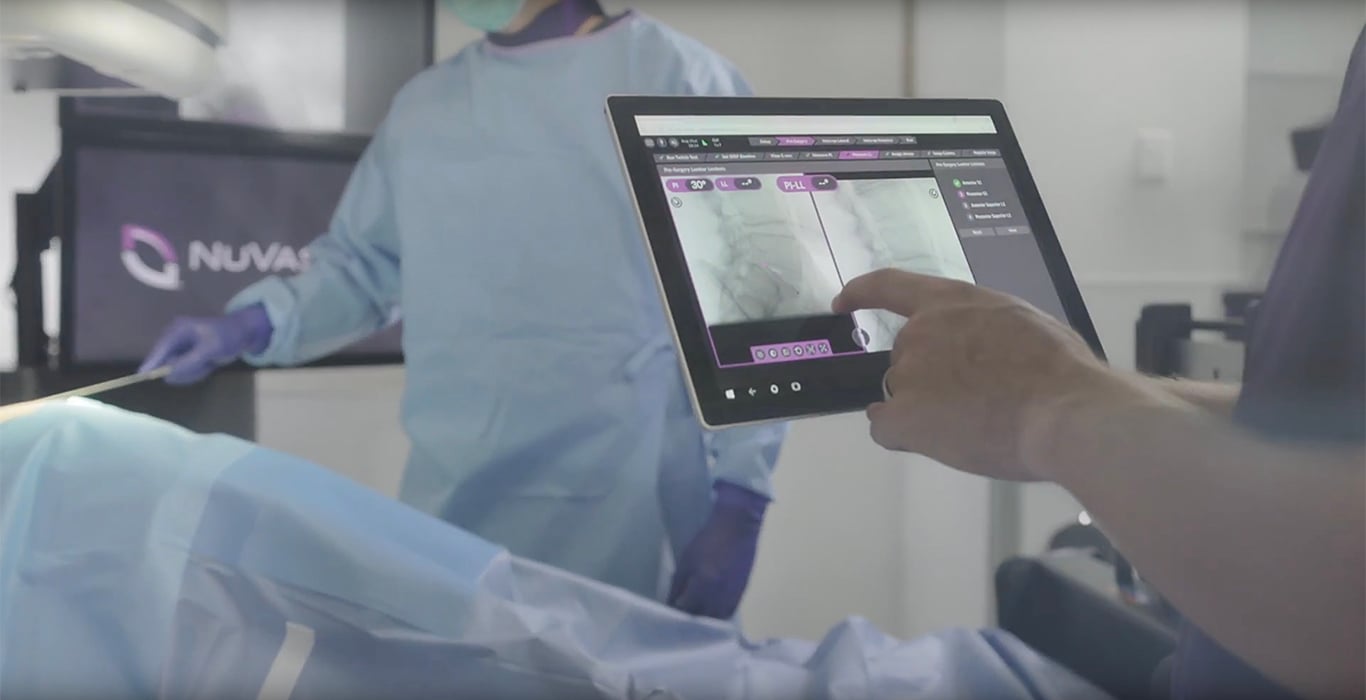 Operating room with screens showing spine and NuVasive logo.