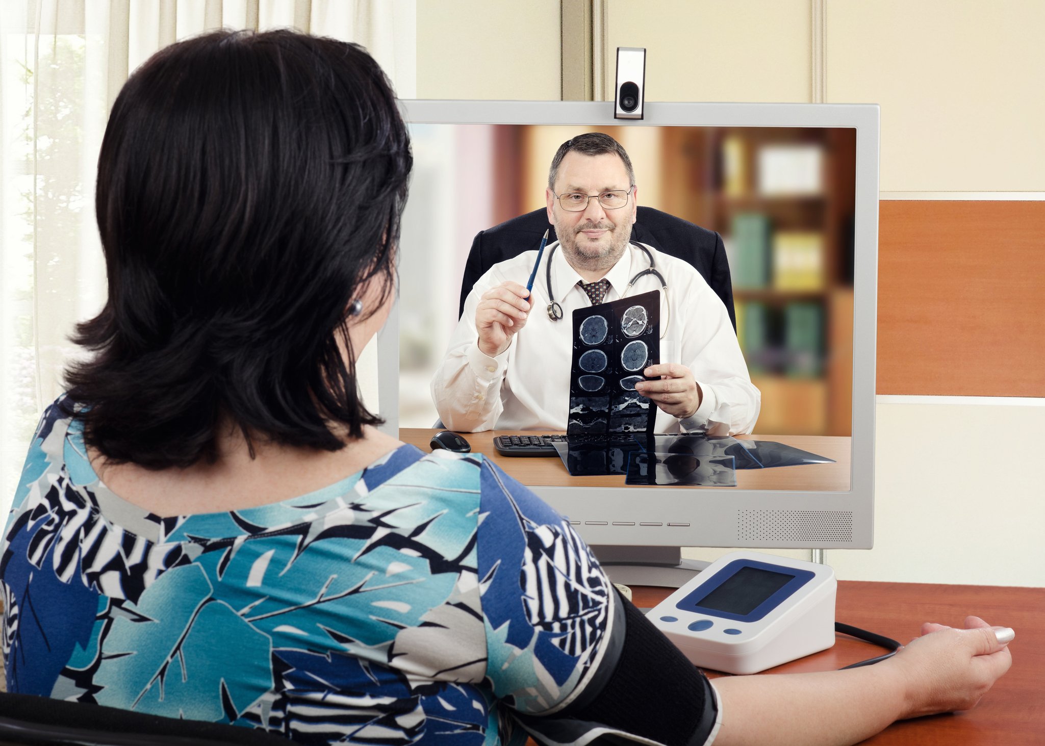 Woman looking at computer screen with a doctor holding an X-ray image