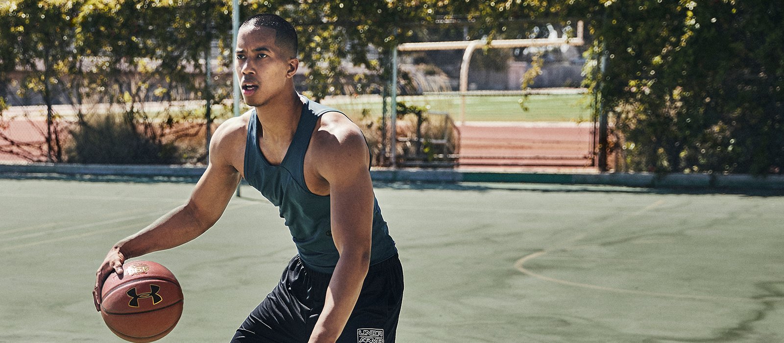 A man dribbling a basketball on a court while wearing Under Armour clothing.