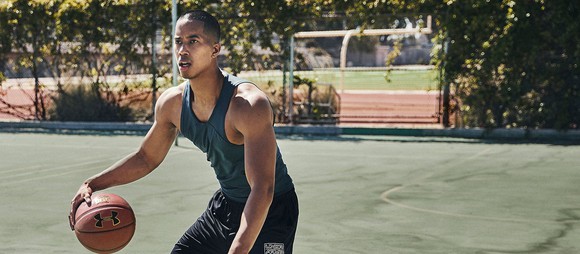 A man dribbling a basketball on a court while wearing Under Armour clothing.