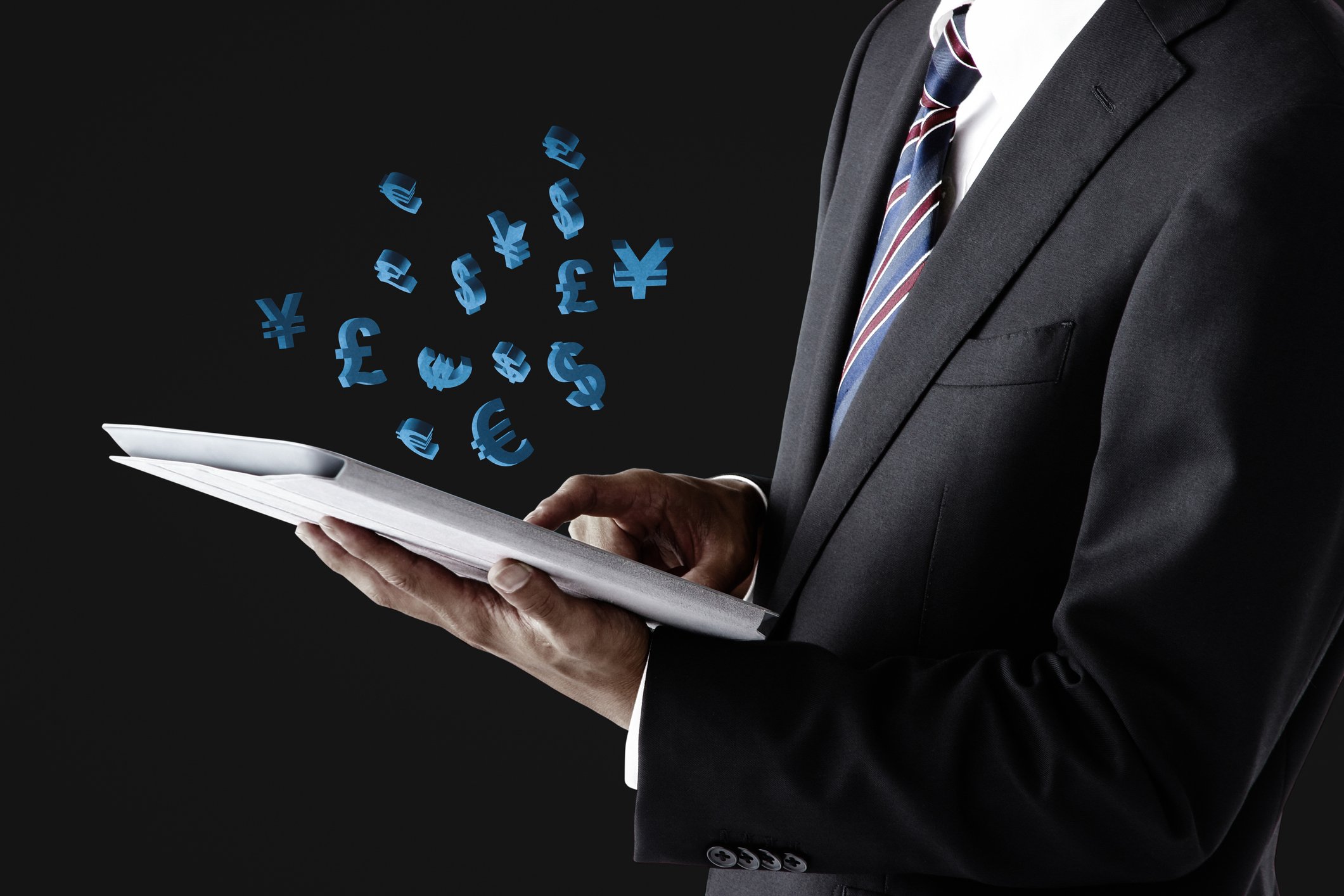 Businessman holding tablet with foreign currency symbols hovering over the screen.