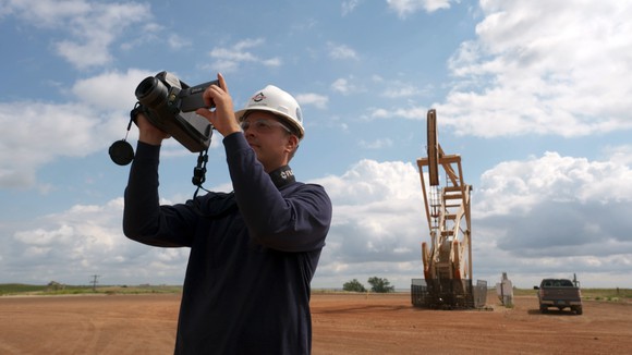 Person holding equipment in front of an oil well.