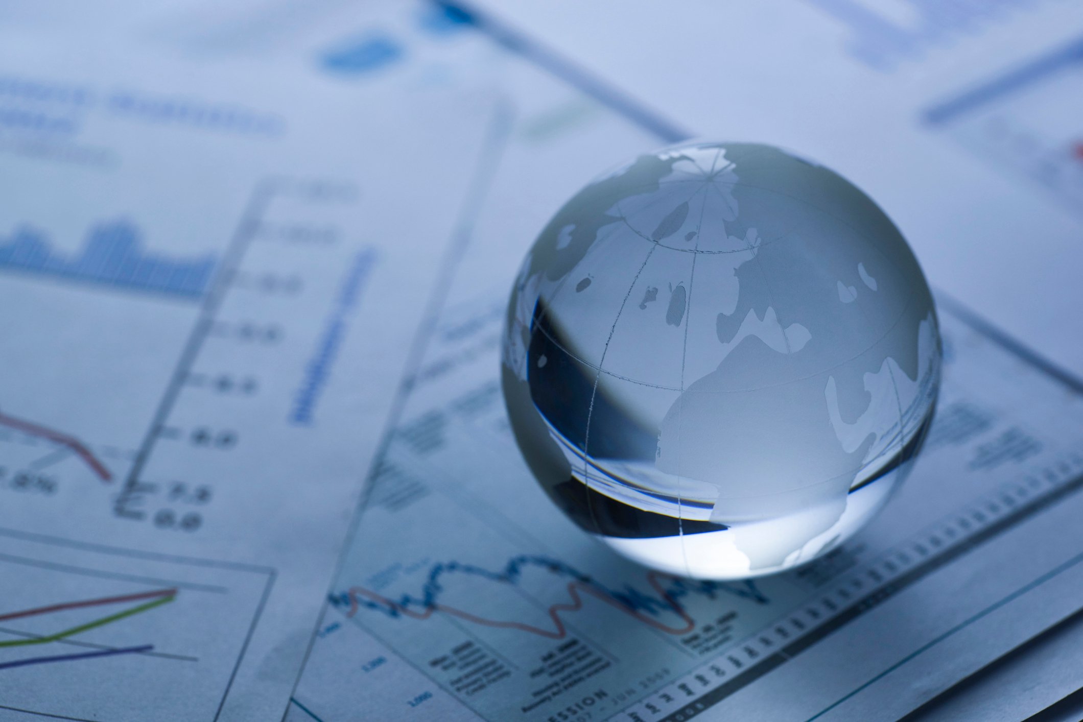 A small glass globe on top of papers displaying graphs and charts