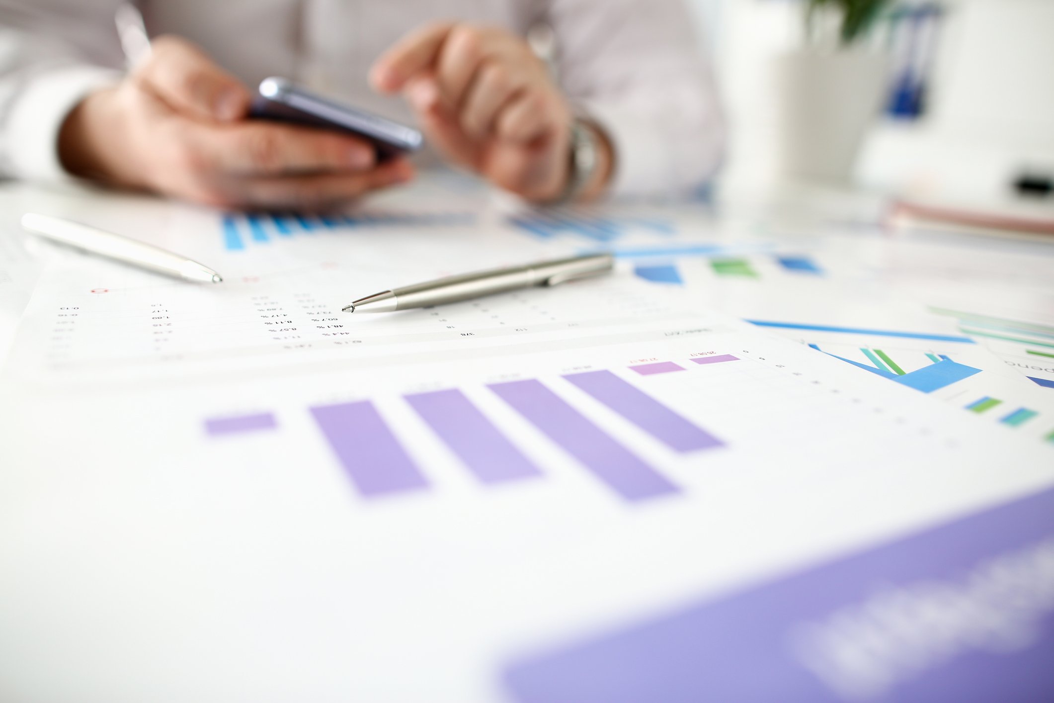 A man holds a smartphone while consulting financial charts.