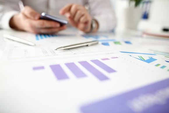 A man holds a smartphone while consulting financial charts.