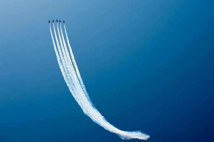 Fighter jets flying in formation and drawing with contrails as they ascend.