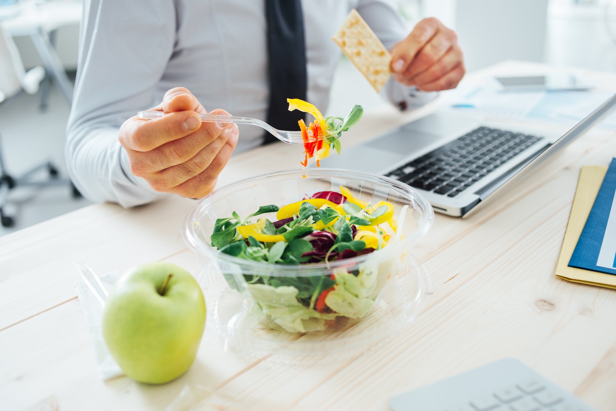 Man eating salad at desk while sitting at laptop