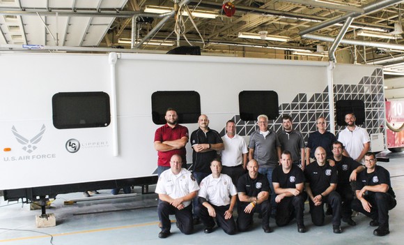 About a dozen people in front of a white RV bearing the Air Force logo.