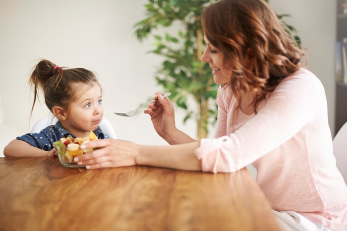 A woman feeding a young girl fruit at the table