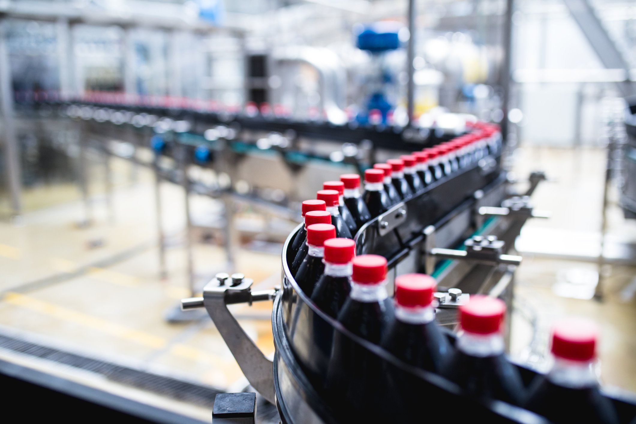 Soda bottles on a curving conveyor belt in a bottling plant.