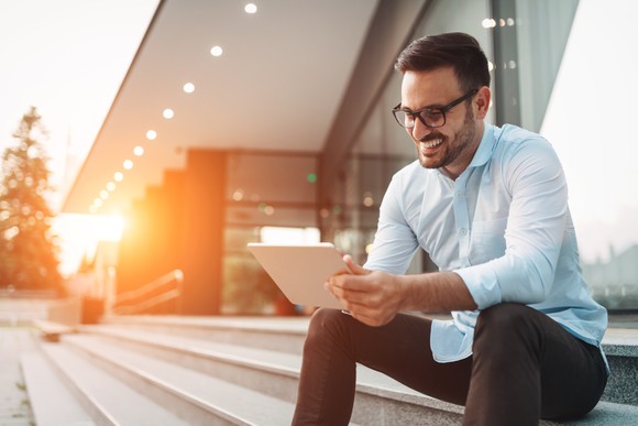 Sitting on steps, a businessman looks at a tablet.