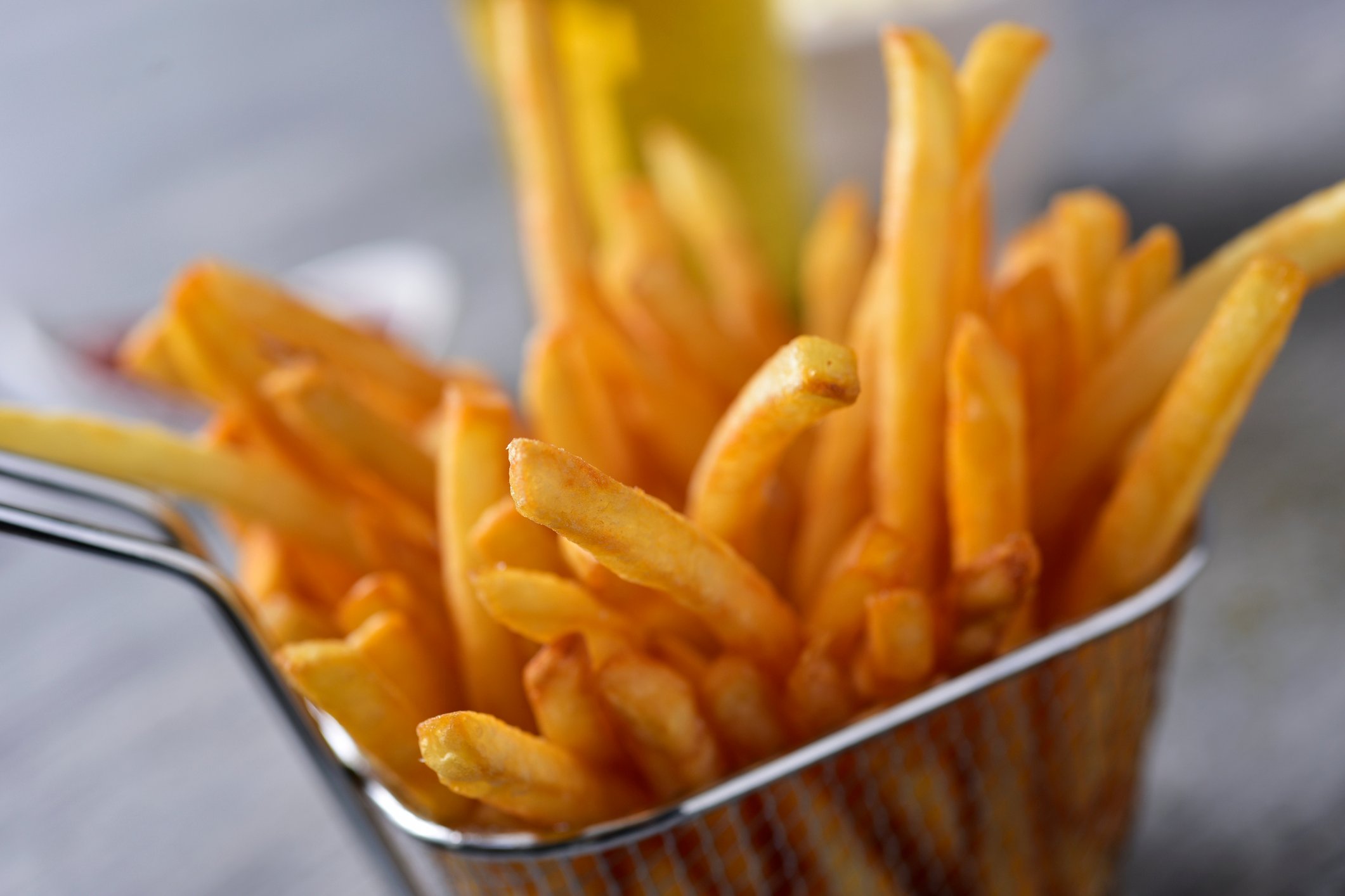 Golden french fries in a small wire basket.