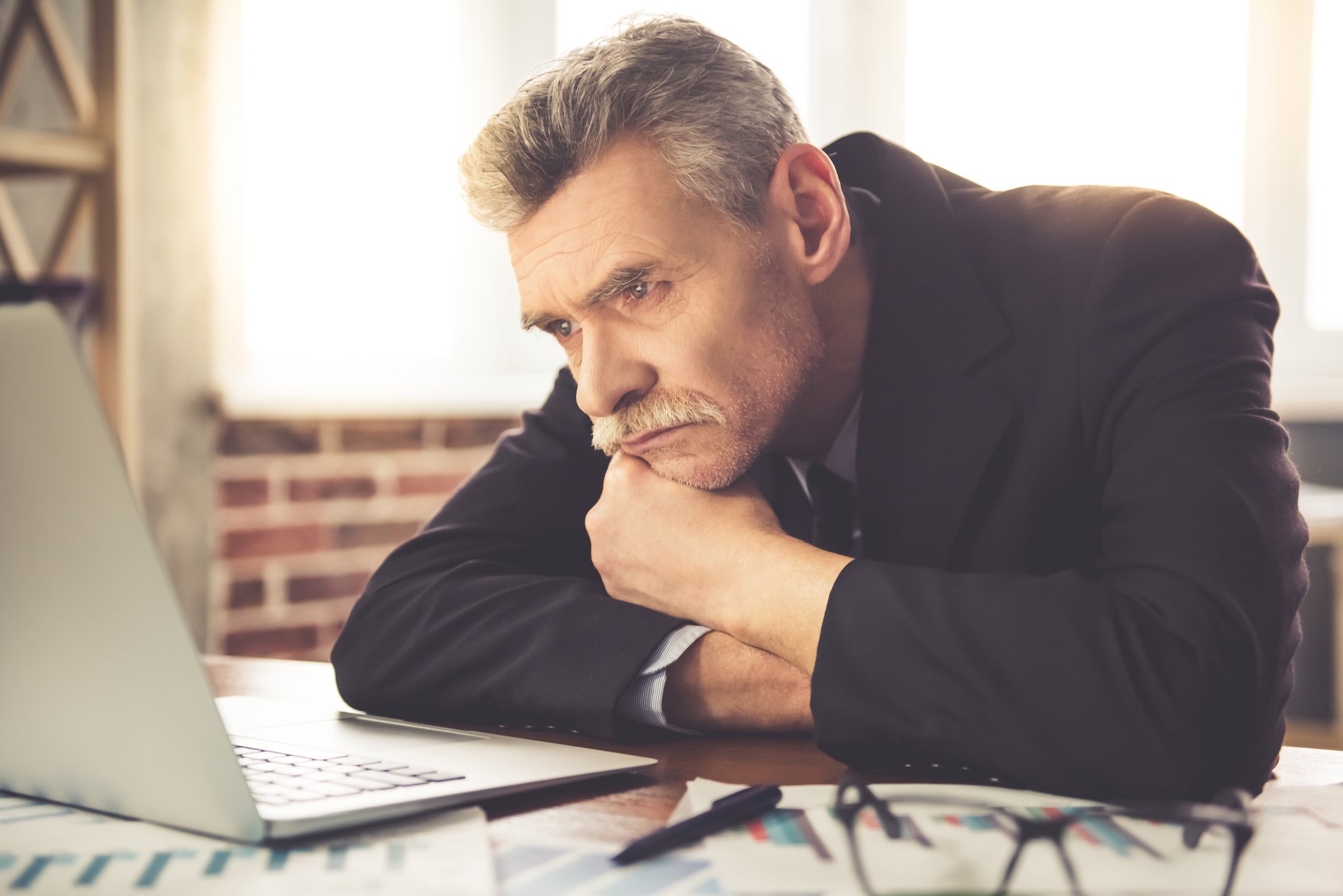 Tired older man in suit looking at a notebook computer.