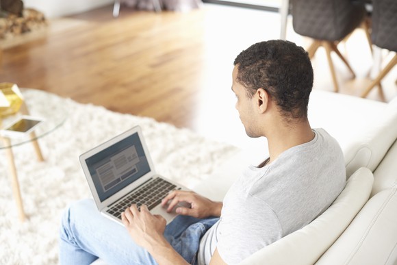 A man types on a laptop on his couch.