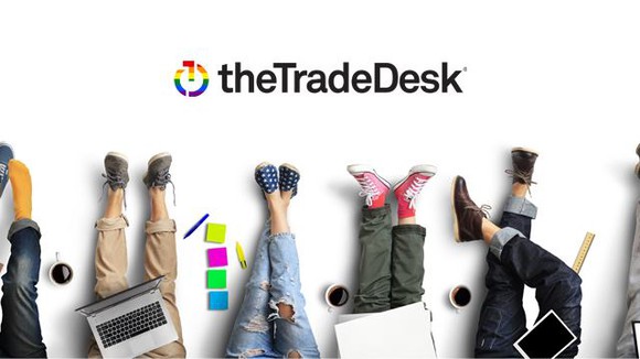 Several legs and feet of people with laptops, on a graphic bearing The Trade Desk's logo