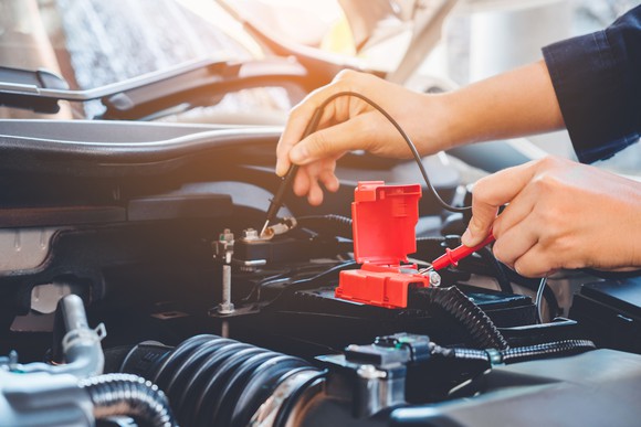 A mechanic in a repair shop tests a car battery's charge.