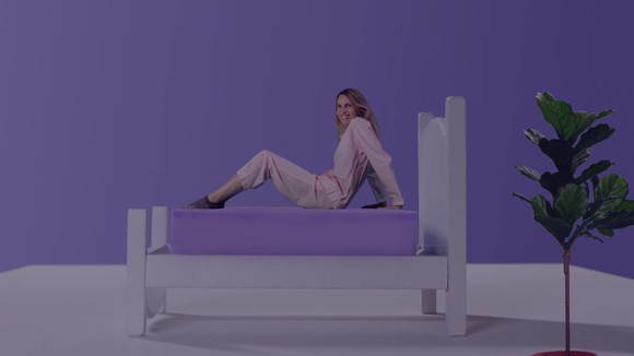 Woman on a bed with a purple mattress, in a room with a purple wall.