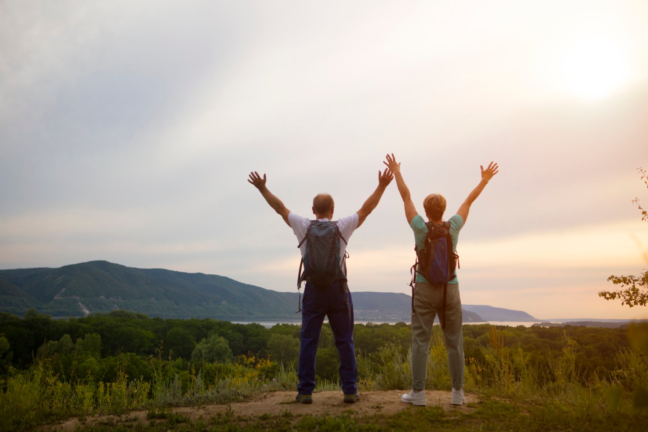 Two hikers standing at a vista with their arms outstretched above their heads