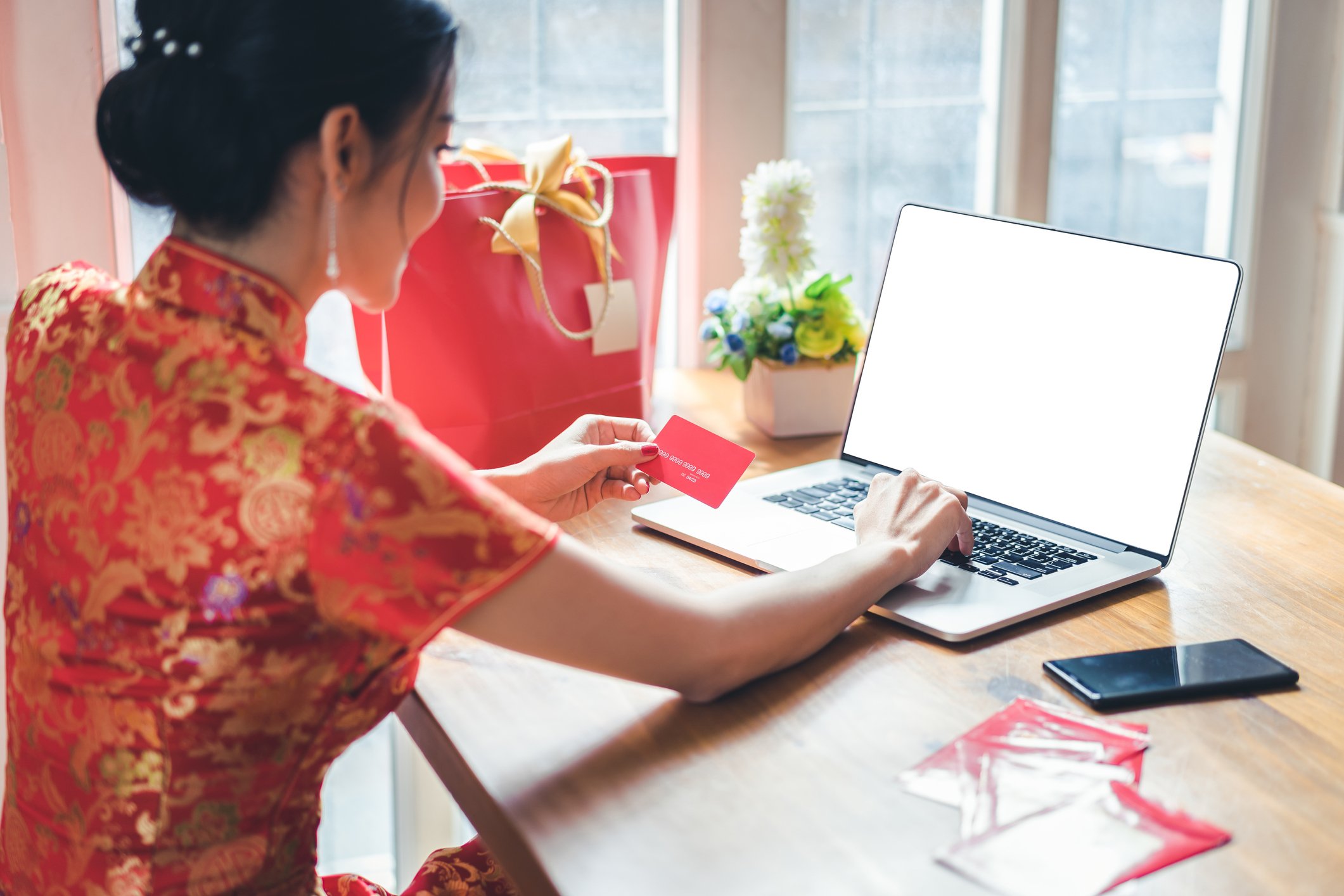 A woman holds a credit card in one hand and types on her laptop with the other. 