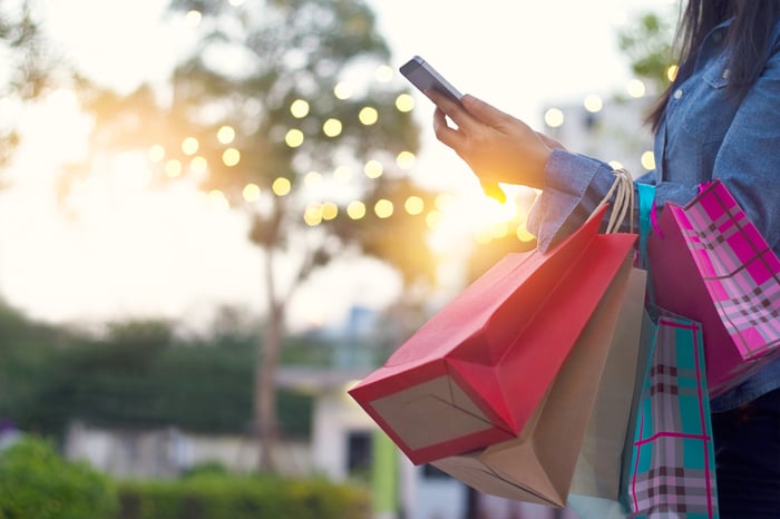 A woman carrying shopping bags uses a smartphone.