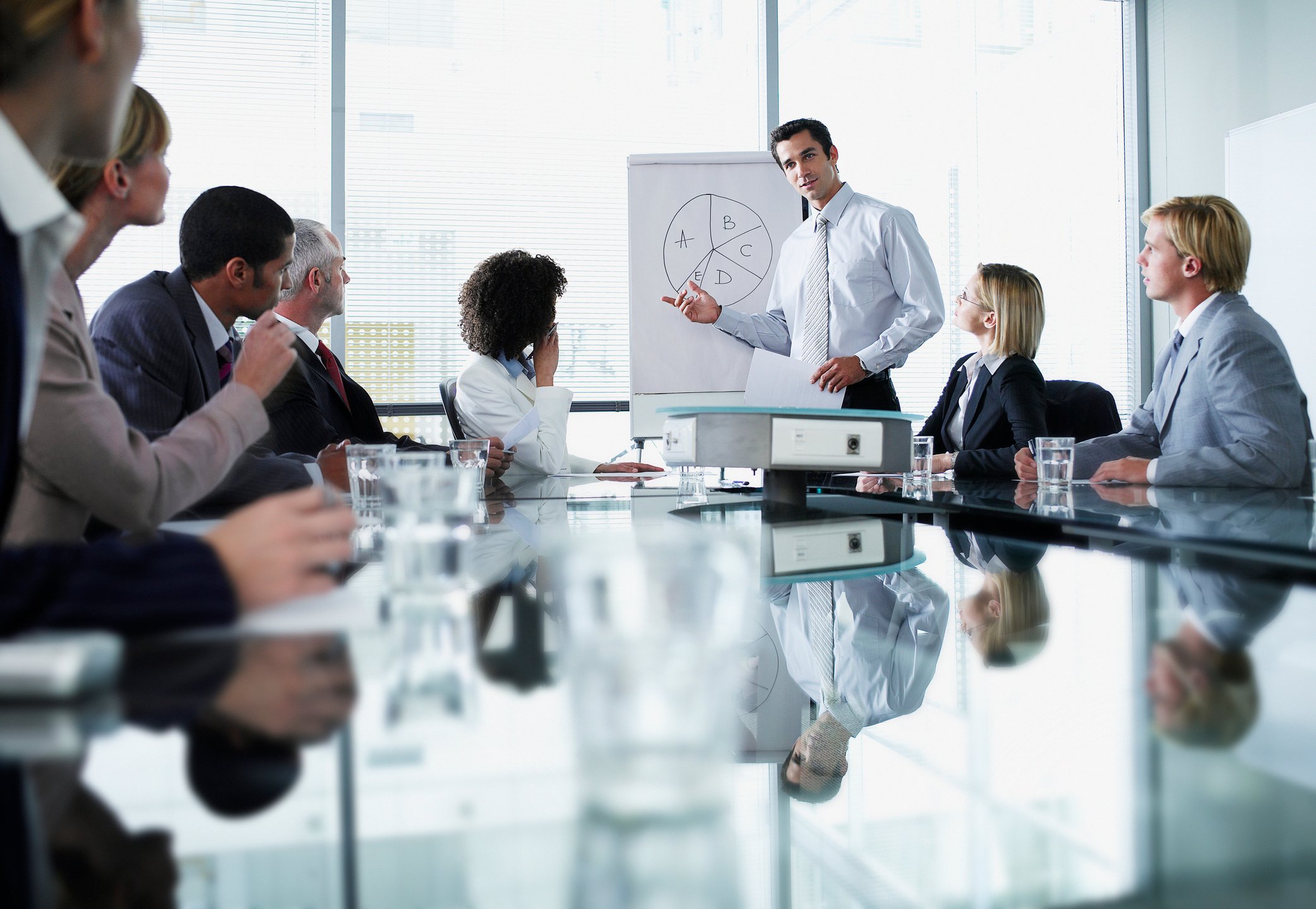 A man leads a presentation around a table in an office setting.