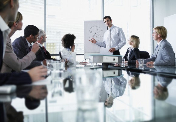 A man leads a presentation around a table in an office setting.