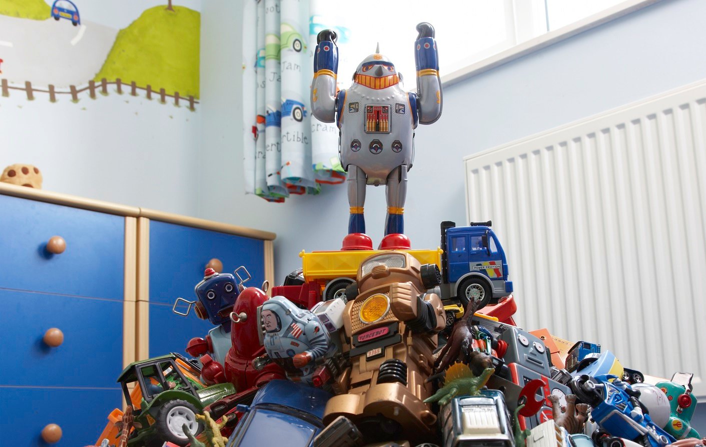 A toy robot stands on top of a pile of toys, its arms raised.