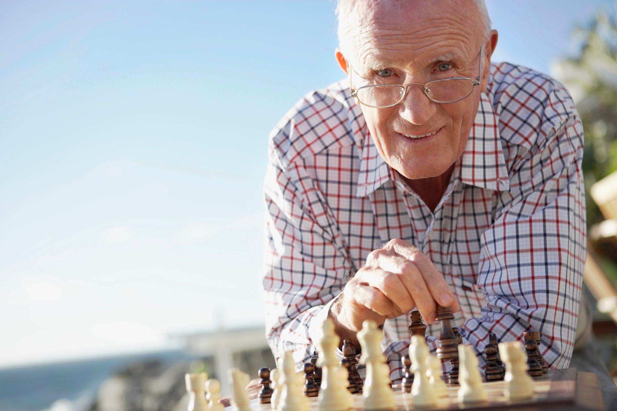 A senior man playing chess near the beach.