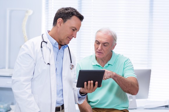 A doctor and patient review information on a tablet in an exam room.