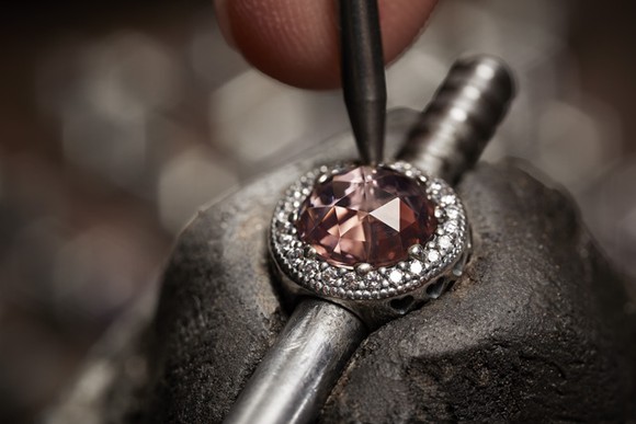 A tool fashions a purple jewel into a circular cubic zirconia setting.