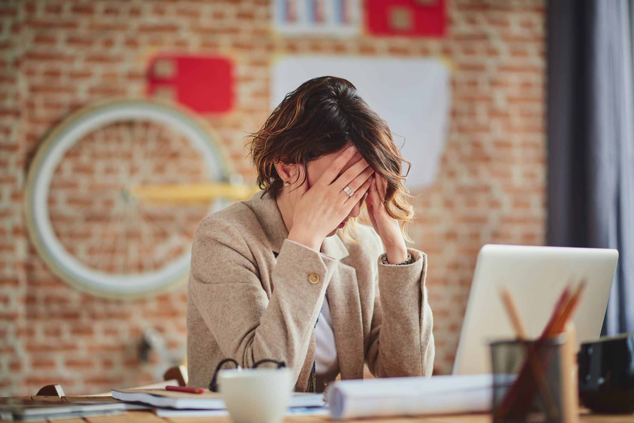 Woman sitting at desk, covering her face with her hands.