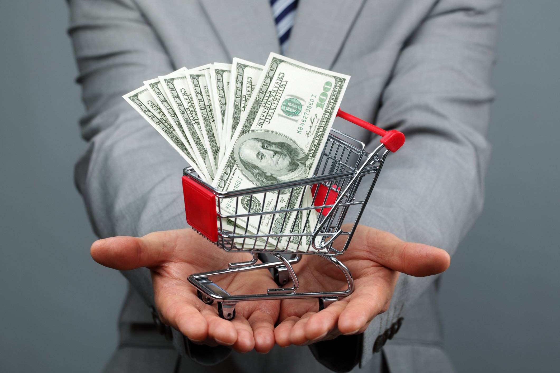 A man in a suit with shopping cart full of money.