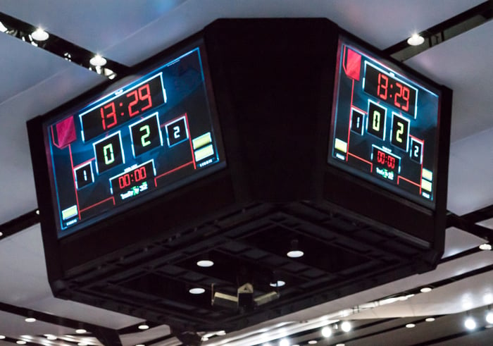 A modern scoreboard, attached to the ceiling of an indoor sports arena.