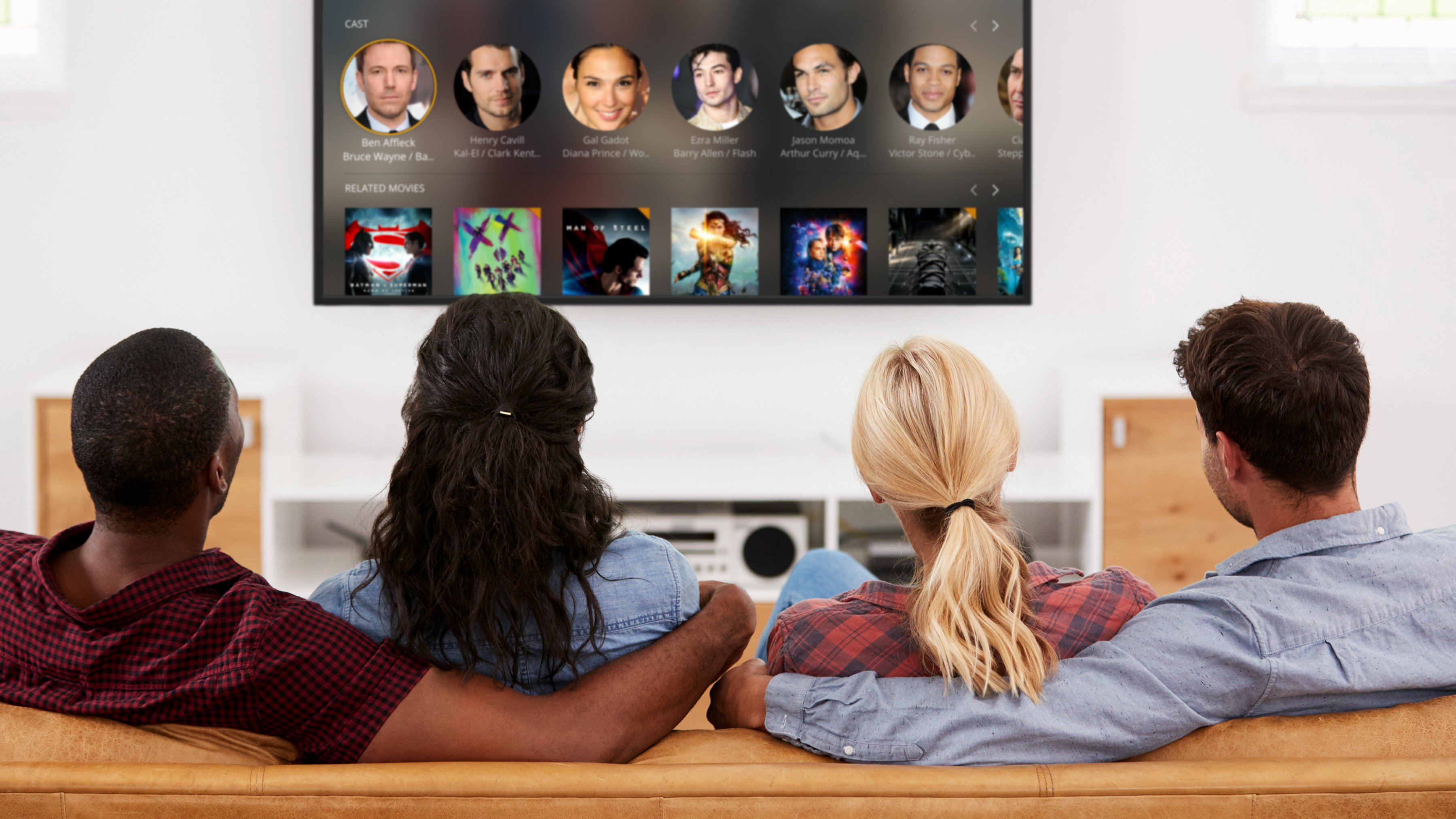 Two men and two women sitting on a couch and watching Plex on a TV