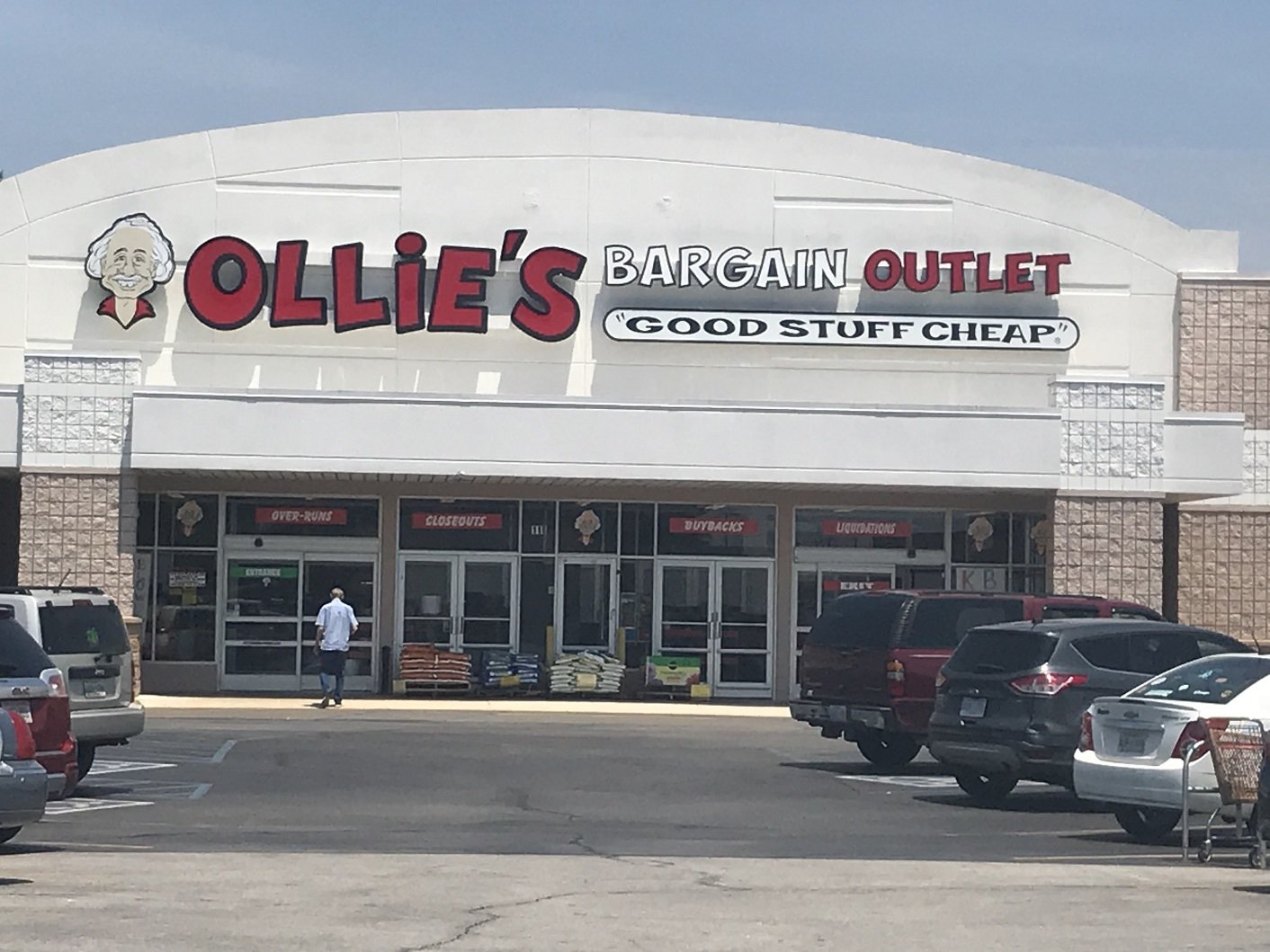 Ollie's Bargain Outlet store seen from parking lot, with several cars and a shopper.