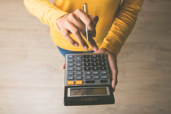 A woman wearing a yellow shirt punching numbers on a calculator.