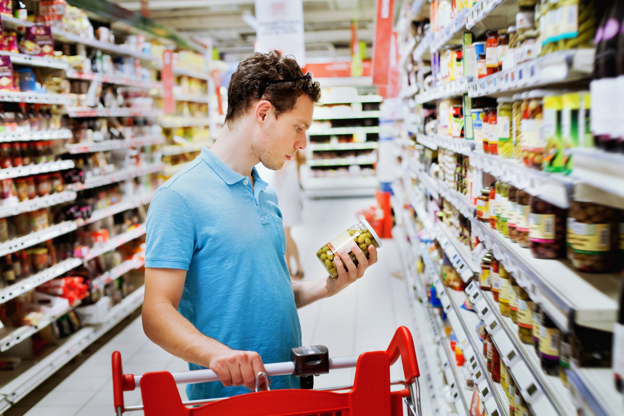 A man examining a jar of olives in the aisle of a grocery store