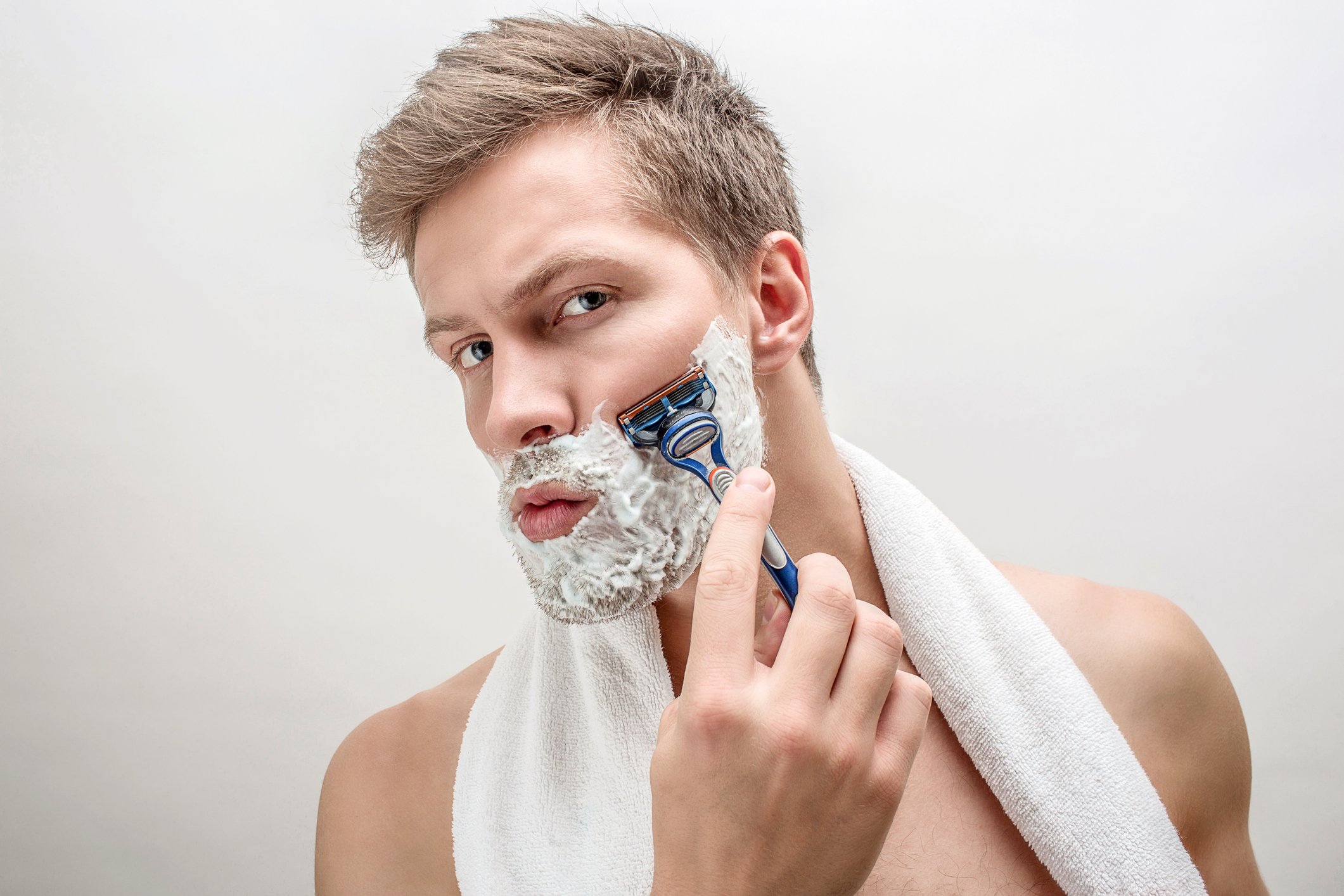 Man shaving with white towel around neck. 