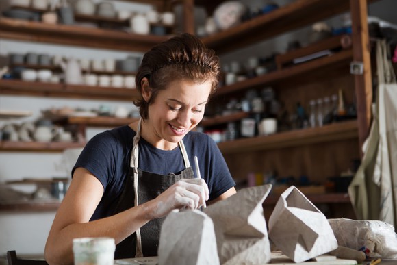 Smiling woman crafting pottery in a well-stocked workshop.