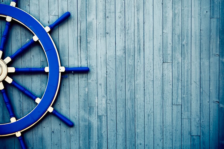 An antique boat helm wheel painted blue rests on a weathered wooden deck.