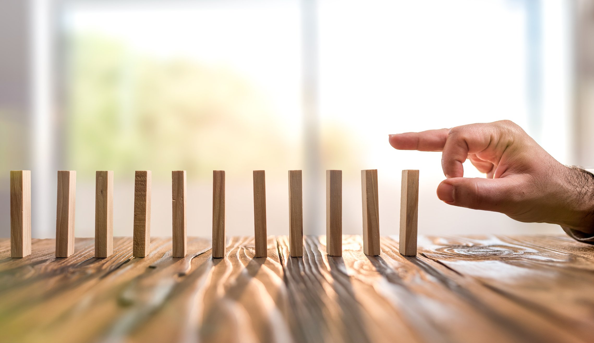 Dominoes lined up with a hand in position to topple the first domino