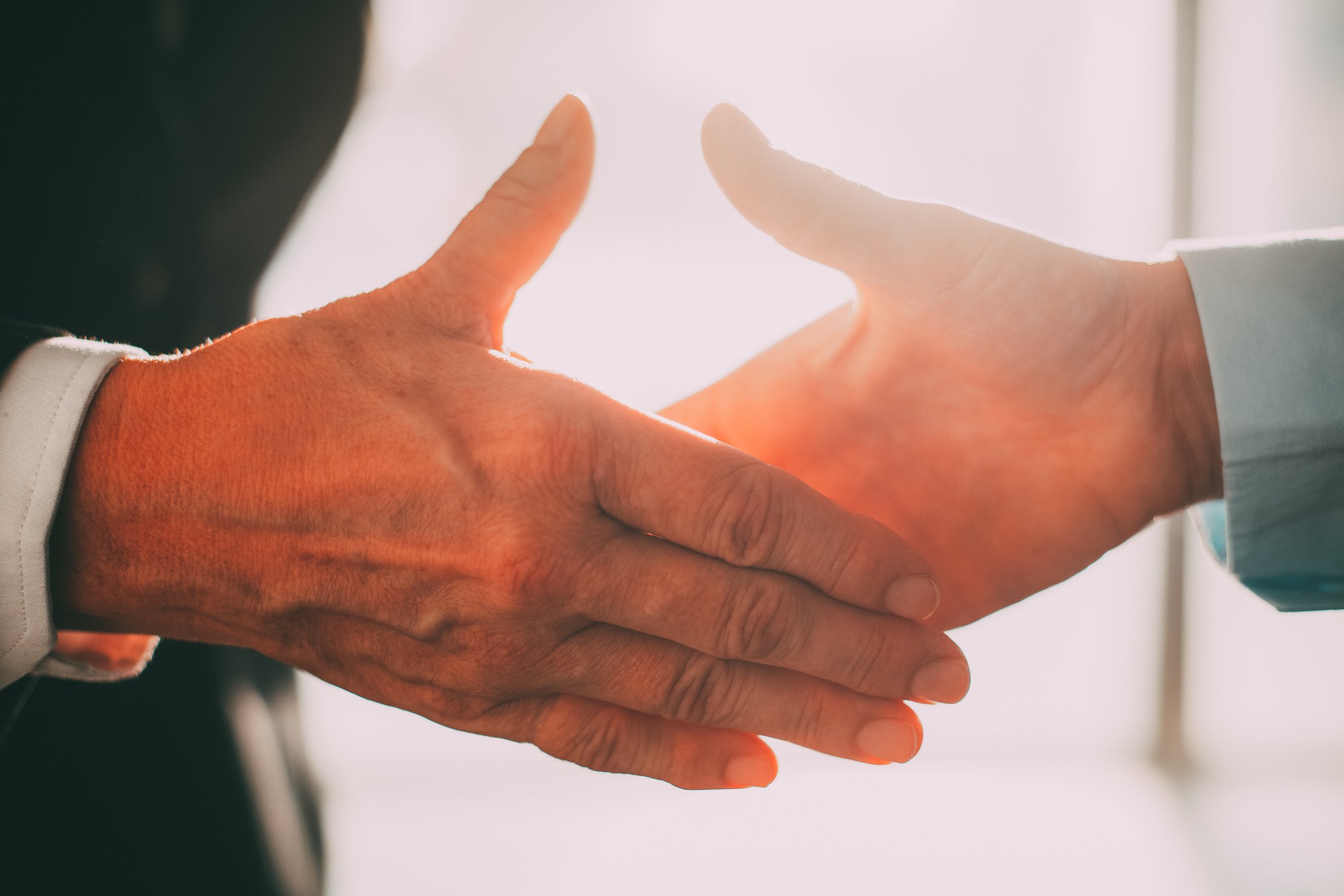 Closeup on a handshake between two businessmen, right before the two hands make contact.