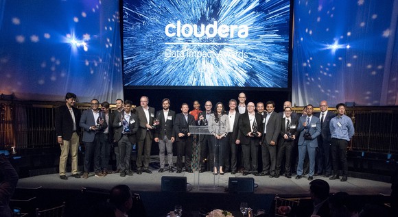 Screen showing Cloudera logo above group of 20 people on a stage.