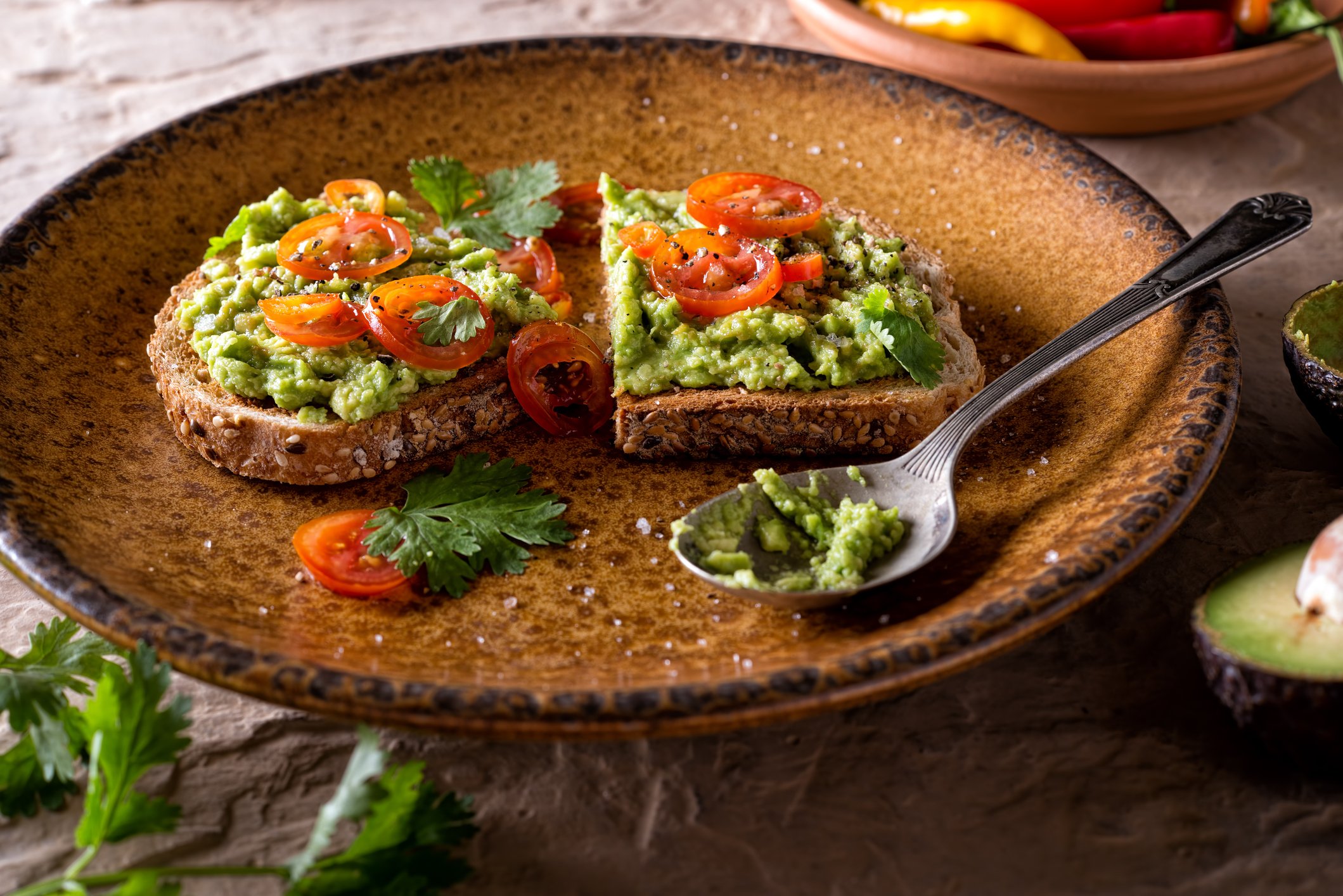 Avocado toast topped with sliced tomatoes in an attractive ochre porcelain bowl.