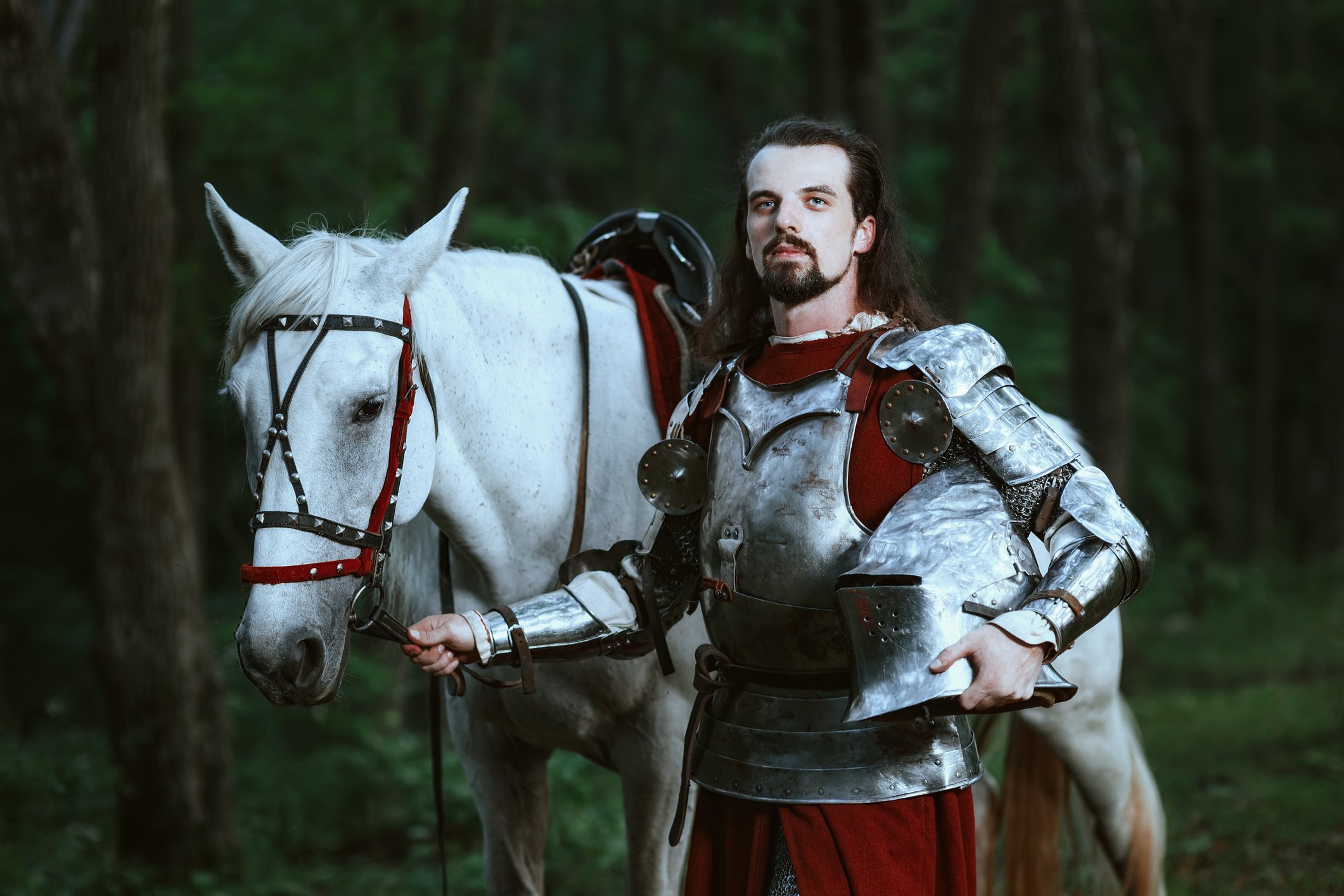 Knight in armor posing next to a white horse