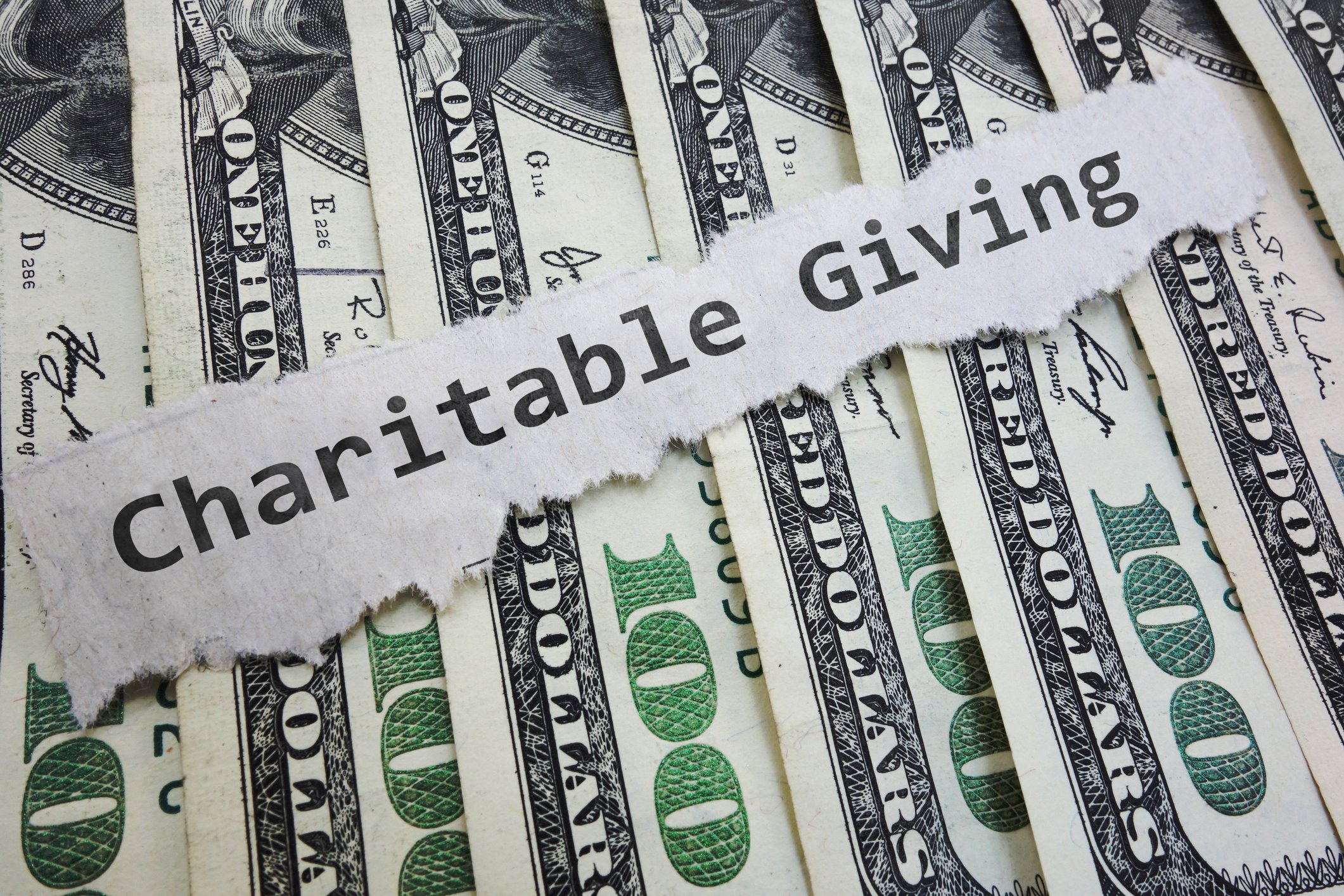 Hundred dollar bills under the words Charitable Giving on a piece of paper.